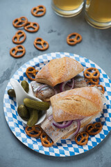 German fish sandwiches with herring fillet on a blue and white carton plate, vertical shot on a grey concrete surface with beer mugs in the background