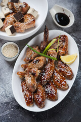 Baked teriyaki chicken wings served on a white plate, vertical shot on a dark grey stone background