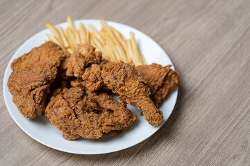 Crispy fried chicken with french fries in white plate on a wooden table.