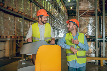 Warehouse workers in orange helmets standing near shelves and talking