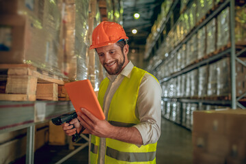 Warehouse worker in yellow vest looking at the tablet and smiling