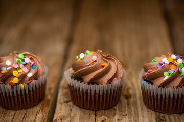 Tasty chocolate cupcakes with sprinkling on rustic wooden table background. Sweet dessert. Bakery concept. Elegant food. Sweets for coffee or tea. Space for text. View from above.