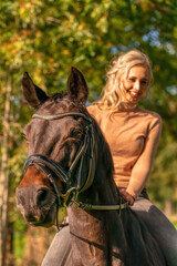 Portrait of a blonde girl on a brown horse. Selective focus on horse