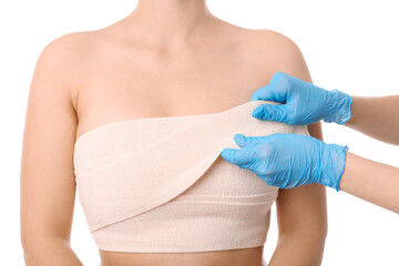 Doctor applying bandage on female chest after cosmetic surgery operation against white background