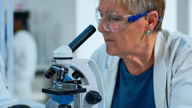 Woman research scientist looking at samples under microscope in modern equipped laboratory. Eldery doctor working with various bacteria, tissue and blood tests, pharmaceutical research for antibiotics