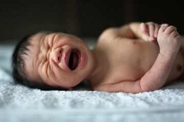 Newborn baby boy crying on the bed
