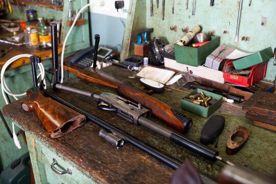 Workplace of gunsmith in professional weapons workshop with tools and disassembled shotgun during repair or maintenance.