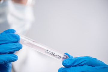 Macro shot of hands in blue protective gloves holds biological tube with label covid-19 on white background. Research and development concept.