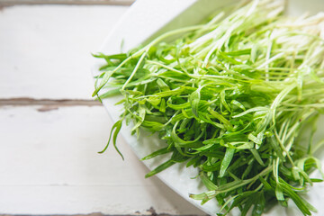 Close up organic water spinach  in a white plate on wooden table next to the window.