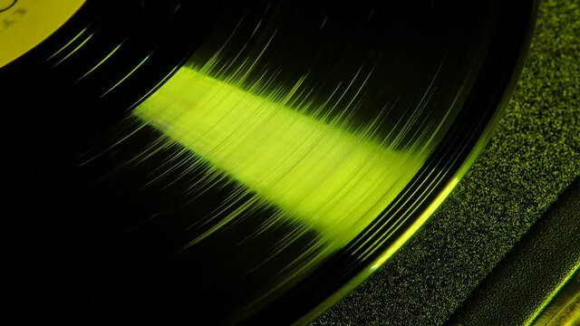 Macro footage of a slow motion spinning vinyl record hitting a beam of yellow neon light. Old retro gramophone playing music. Top view. Close up.