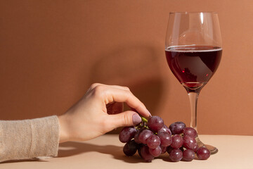 Tender woman hand holds grape near the glass of fragrant red wine. Concept of alcoholic drinks. Dessert.
