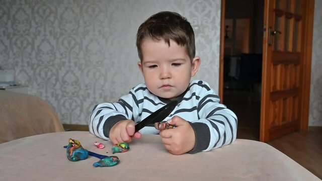 Serious little boy cuts plasticine and tries to eat it, Child hands playing with colorful clay, day care close up, tactility activity.
