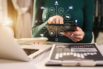 Designer using tablet with laptop and document on desk in modern office with virtual interface graphic icons network diagram.