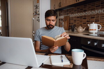 Attractive young hipster man focused reading book at home office