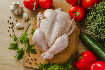 Raw chicken on the cutting board. Flat lay composition with tomatoes, bell peppers, green parsley, garlic, cucumber and allspice. Preparing dinner for Thanksgiving or Christmas.