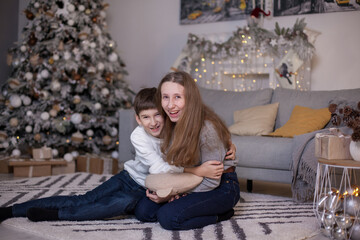 happy brother and sister sitting on floor near sofa and christmas tree with presents and looking at camera. Boy and girl at Christmas time. Merry Christmas and Happy New Year