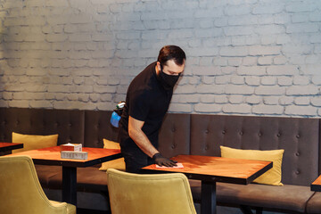 Waiter wearing protective face mask and gloves while disinfecting tables indoor restaurant, cafe. Precautions during the covid-19 coronavirus pandemic - Powered by Adobe