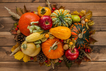 Variety of edible and decorative gourds and pumpkins. Flat lay composition of different squash types with cones, nuts, corn on the cob, kaki, rosehips, physalis peruviana fruits and autumn leaves.