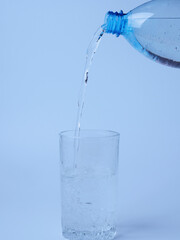 Pouring water from a bottle into a glass on a blue background