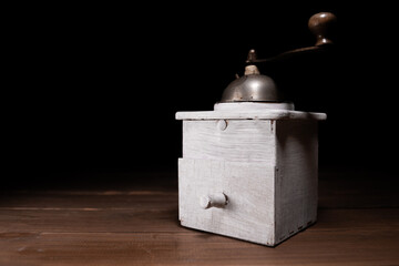 Vintage retro manual coffee grinder on a wooden table, with black background.