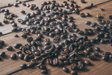 Roasted unground coffee beans, covered with smoke on a wooden table.