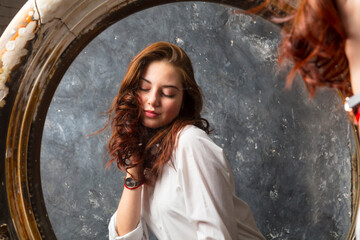 Beautiful young woman looking on her reflection at retro style mirror.