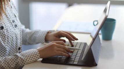 Female hands typing on tablet keyboard on white worktable with coffee mug