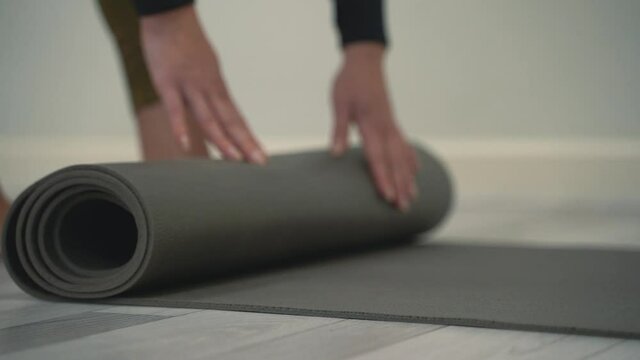 Young woman unrolls yoga mat on floor and prepares to meditate and do exercises. Close-up.