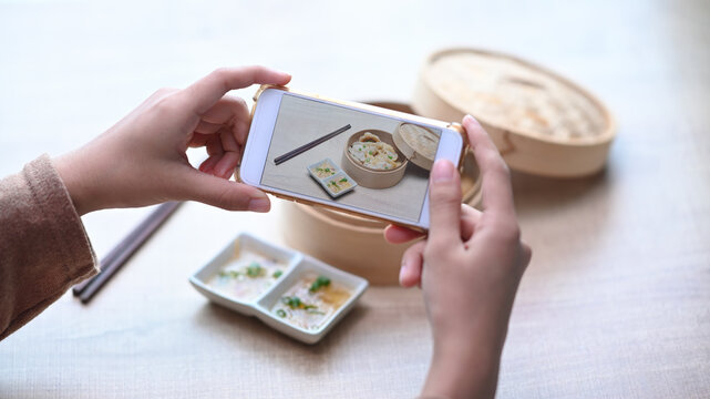 Woman using smart phone taking photo of original Japanese dumplings on wooden table.