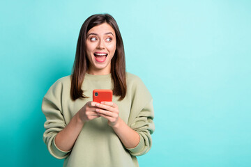 Photo portrait of amazed screaming woman holding phone in two hands looking at blank space isolated on vivid turquoise colored background