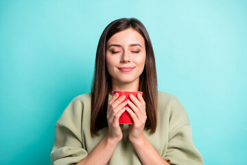 Photo portrait of woman inhaling aroma of nice coffee holding red cup in two hands with closed eyes isolated on vivid turquoise colored background
