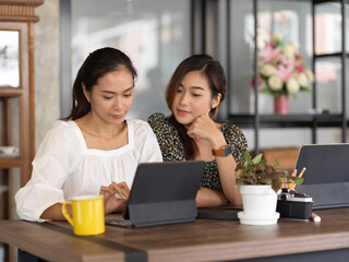 Female teenagers doing homework together with digital tablet in cafe