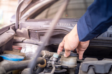 Repairman is examining the coolant-level radiator in the engine. Auto mechanic working on car engine in mechanics garage.