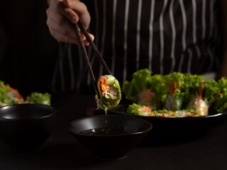 Female cook gripping  Vietnamese spring rolls with chopstick in dark background