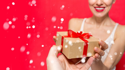 Beautiful woman with gift box over red background with snowflakes