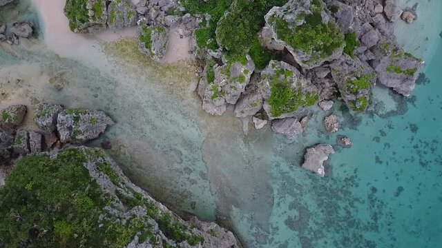 透き通る青い海と緑の映える岩場を見下ろすドローン俯瞰動画（下降）