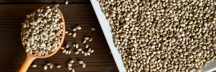 organic dried hemp food seeds in a ceramic plate and rustic wooden spoon on dark wooden background. flat lay. banner