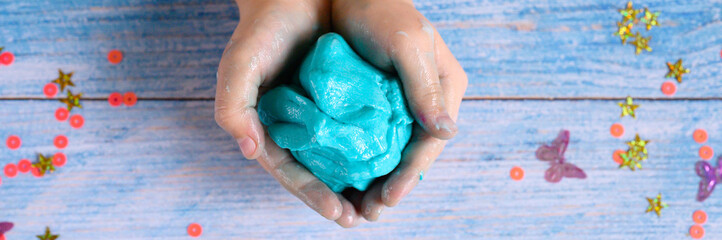 a little girl hands making slime herself on blue wooden background. banner