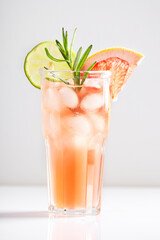 A beautiful alcoholic cocktail of paloma with ice, tequila, lime and grapefruit stands in a glass on a white background. Close-up, horizontal orientation.