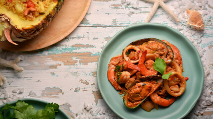 Seafood stir-fried curry powder on green ceramic plate on wooden table, Thai food