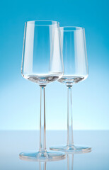 Two empty wineglasses on reflective surface. Studio photo isolated on blue background.