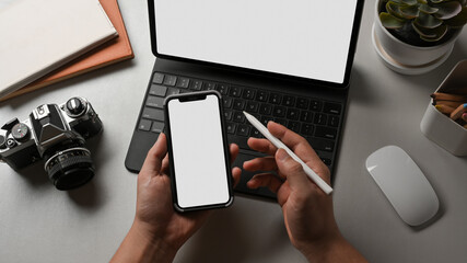 Male hands using smartphone while working with tablet on worktable