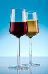 Two glass of red and white wine on reflective surface. Studio photo isolated on blue background.