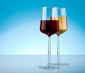 Two glass of red and white wine on reflective surface. Studio photo isolated on blue background.
