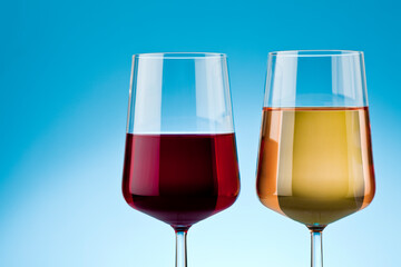 Two glass of red and white wine on reflective surface. Studio photo isolated on blue background.