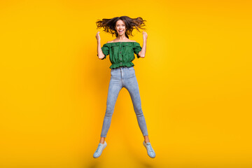 Full length photo of joyful sweet young woman fly hair raise hands jump up air isolated on bright yellow color background