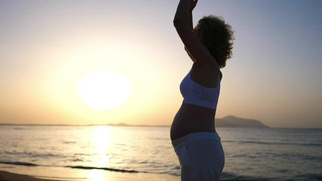 Happy maternity leave on beach. White pregnant woman practicing sunset yoga at seaside 