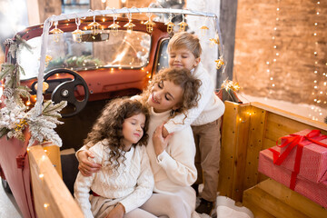Happy family. Mother hugging her little children on Christmas holidays, with lights in red car pickup trailer © Marharyta