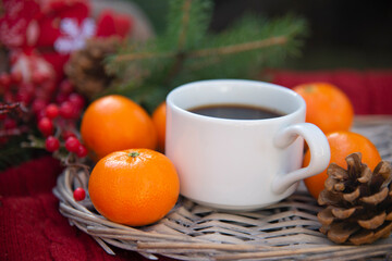 Obraz na płótnie Canvas A white Cup of coffee on a background of Christmas decorations and orange tangerines. Christmas background with hot drink