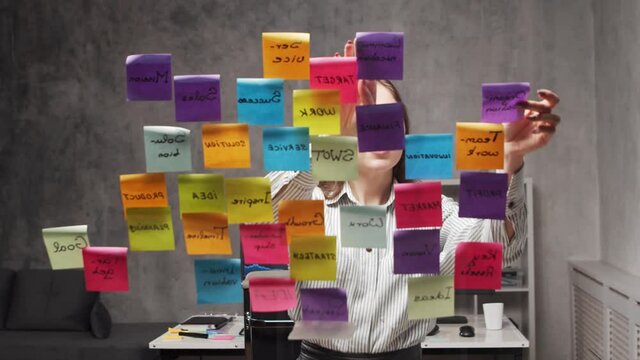 Timelapse of the young business woman doing brainstorm using stickers on the glass. Office worker is thinking about strategy, business plan and goals. Startup concept.